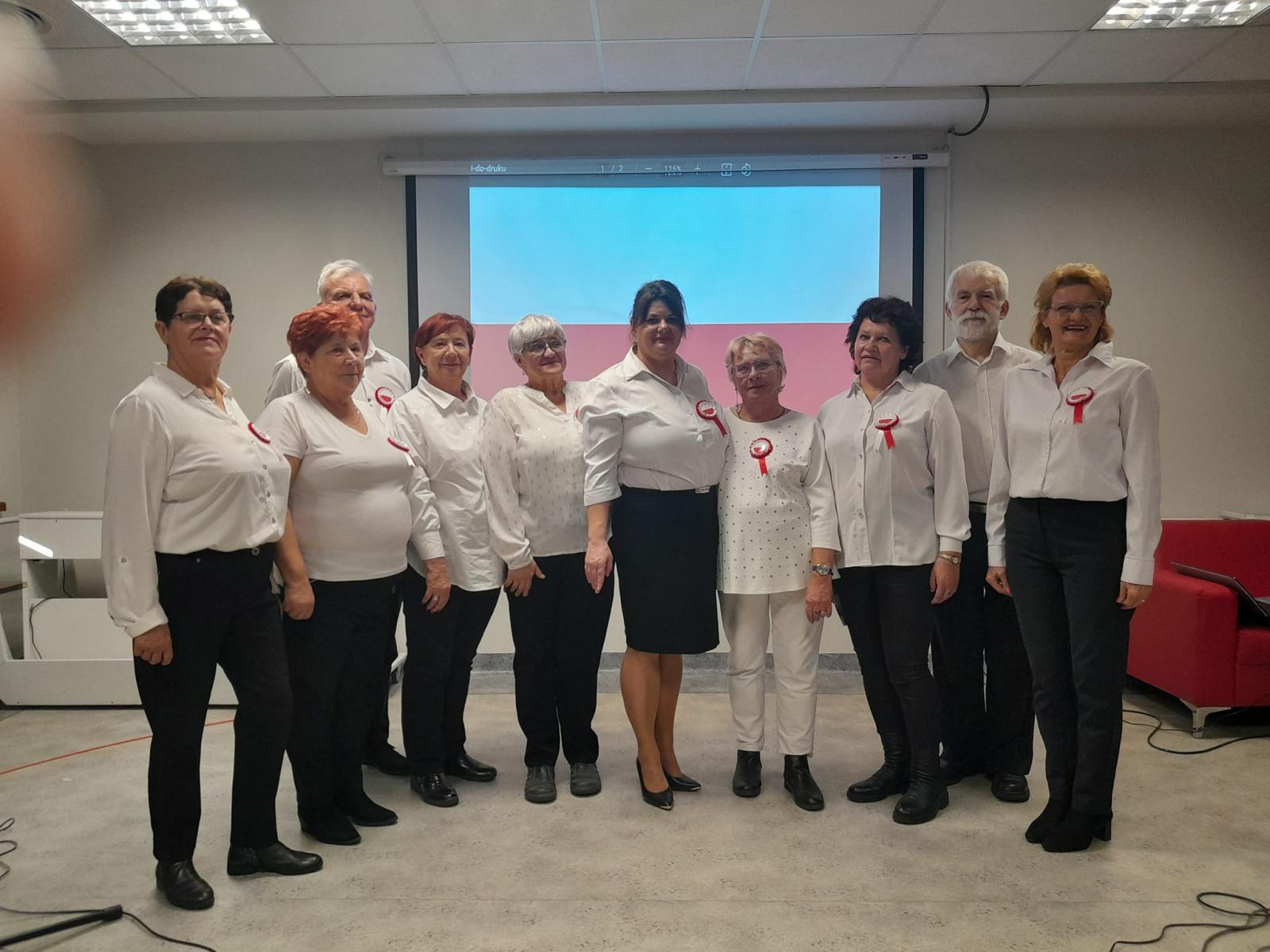 Seniorzy z Domu Sąsiedzkiego śpiewają hymn Polski elegancko ubrani.