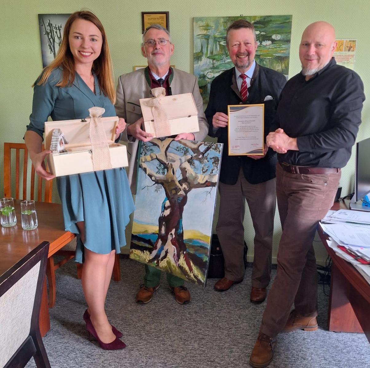 Dyrekcja MOPR stoi z podziękowaniami z przedstawicielami Joannit&oacute;w z Niemiec, daje prezenty: obraz, drewniane skrzyneczki i podziękowania w ramce