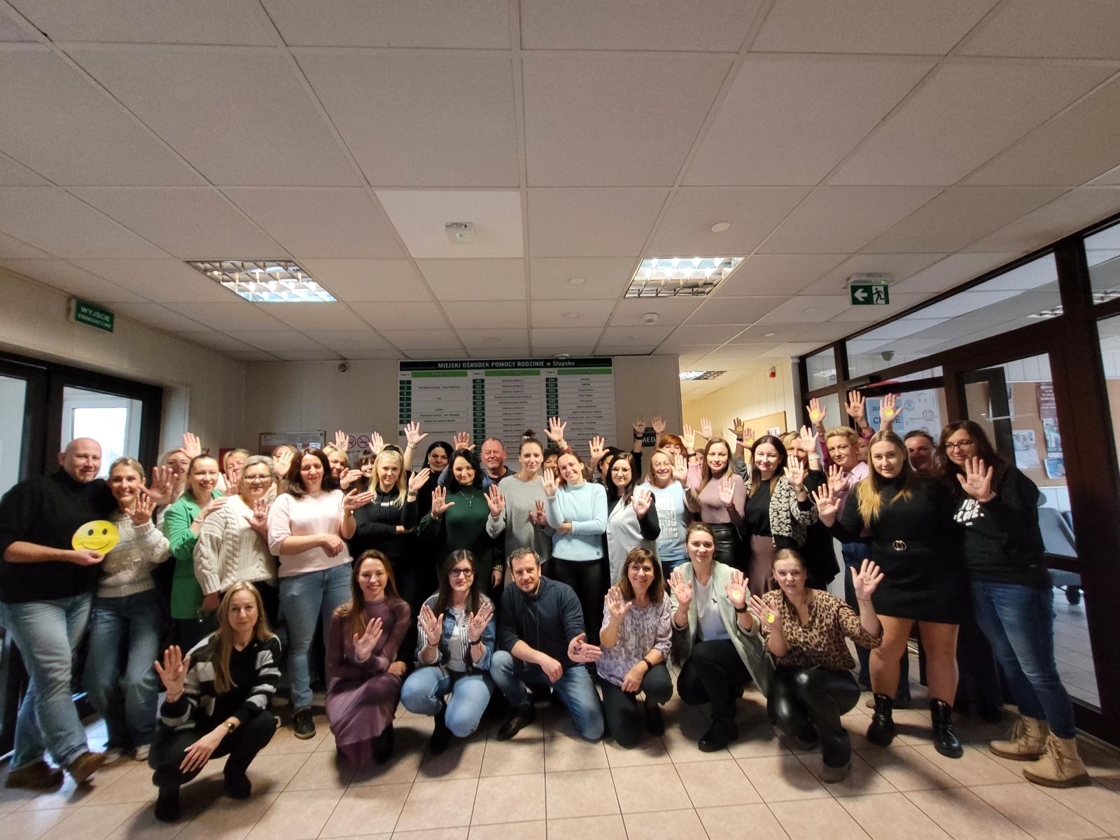 Grupa pracownik&oacute;w MOPR uśmiecha się i pokazuje symbol Dnia Adopcji namalowaną buzię na dłoni