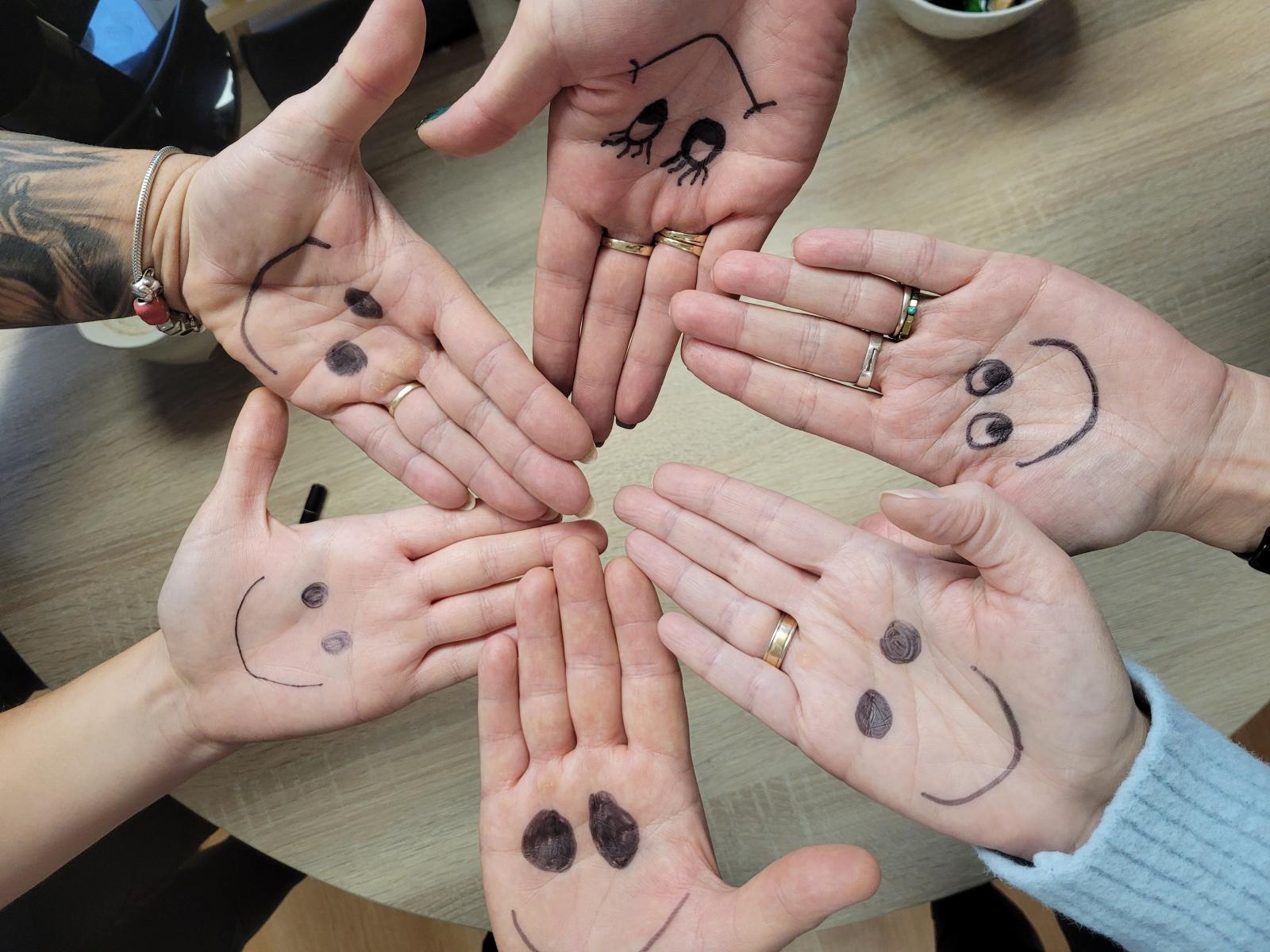 Pracownicy pokazują dłonie na kt&oacute;rych namalowany jest symbol Adnia Adopcji uśmiechnięta buzia